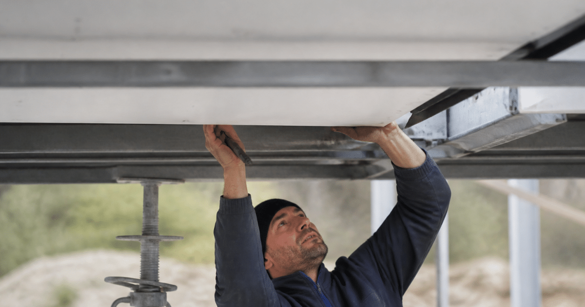 Ouvrier fixant plaques blanches sous structure metallique suspendue