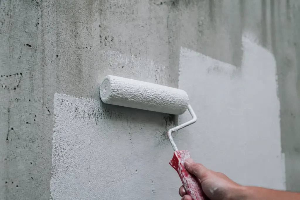 Mur en beton gris et rouleau de peinture blanche